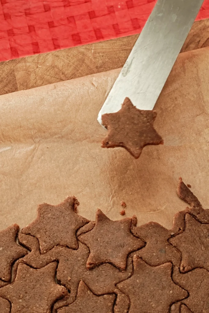 A spatula lifts the freshly cut Cinnamon Star out of the cookie dough.