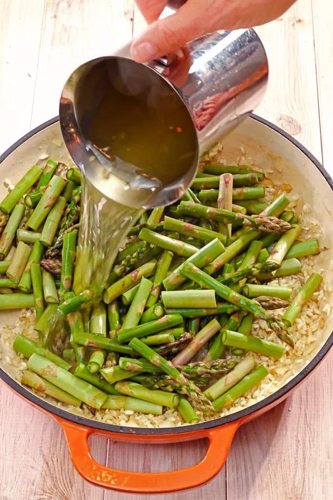 Vegetable broth is added to the pan with green asparagus and risotto rice.