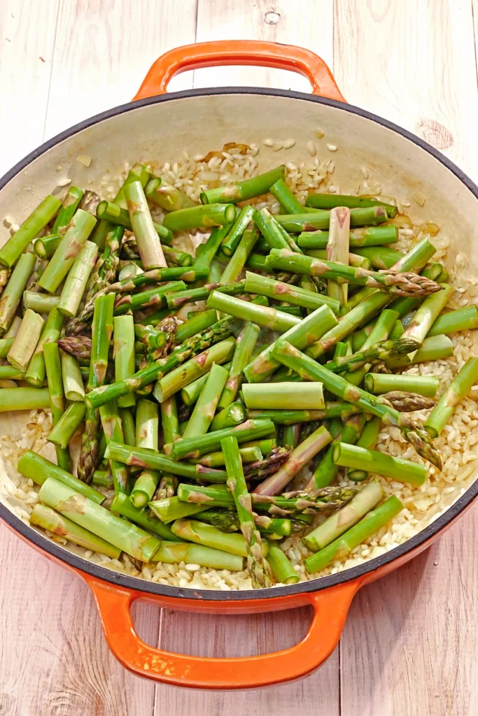 In a high pan, green sliced asparagus is added to the risotto rice.