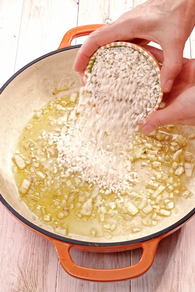 In a high pan, risotto rice is poured into the fried garlic and onion.