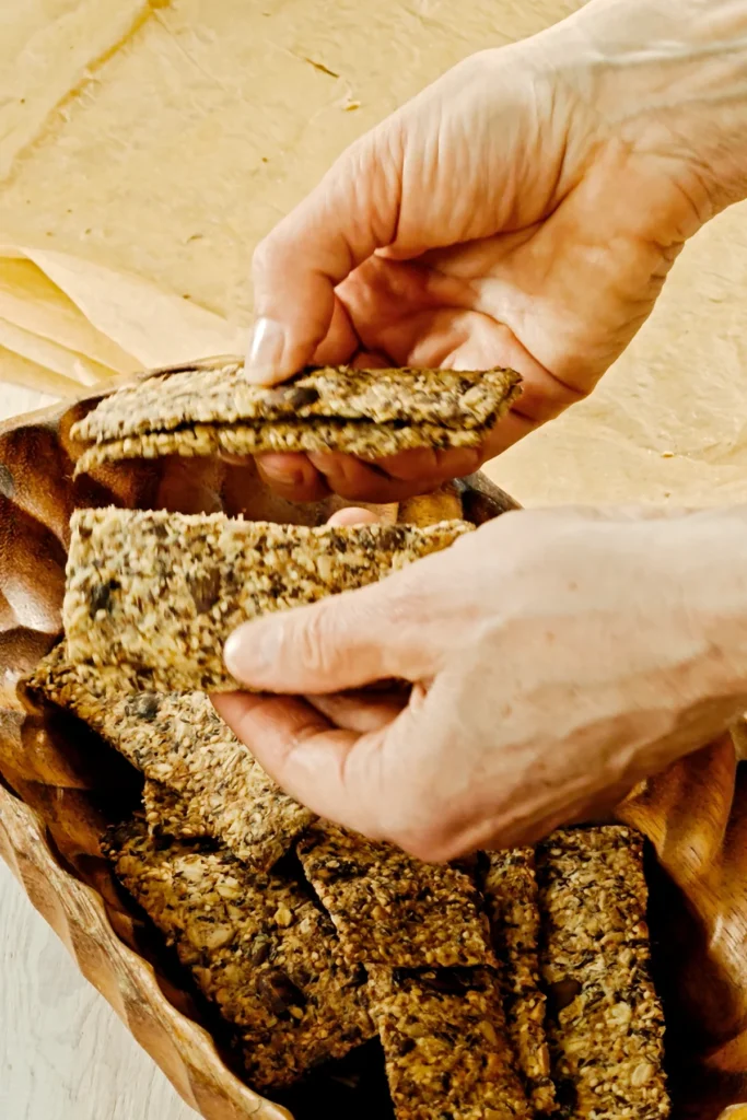 Two hands break the baked crispbread with seeds along the cut edges.