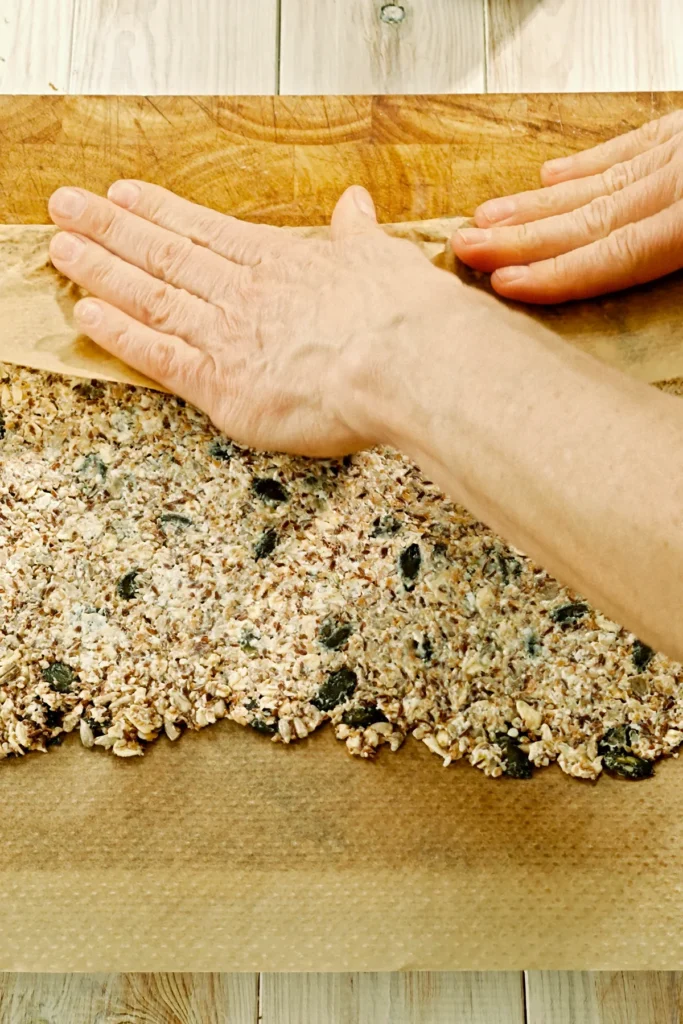 Hands fold the baking paper over the outer edge of the rolled out crispbread dough to form a smooth edge.