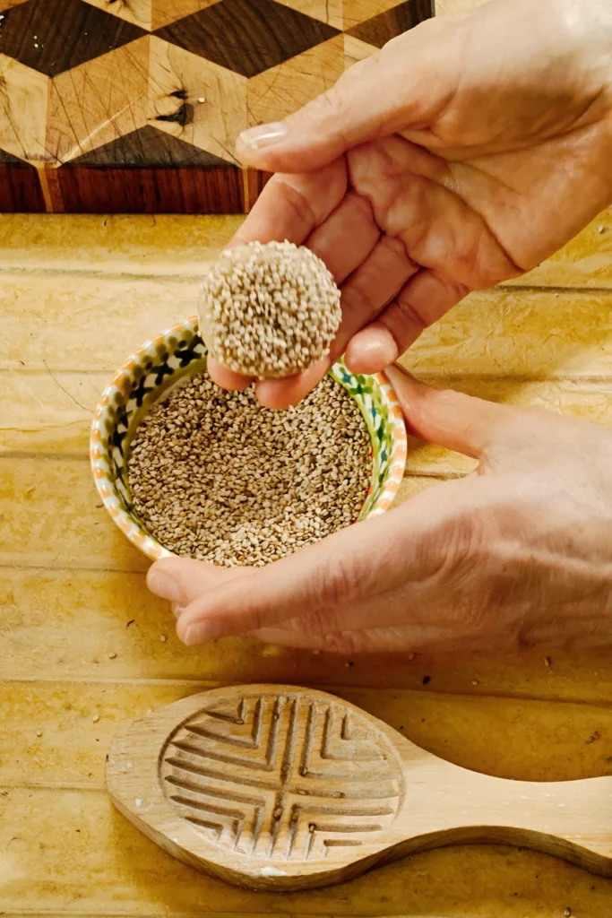 The rolled cookie with marzipan filling is pressed into a bowl with sesame seeds.