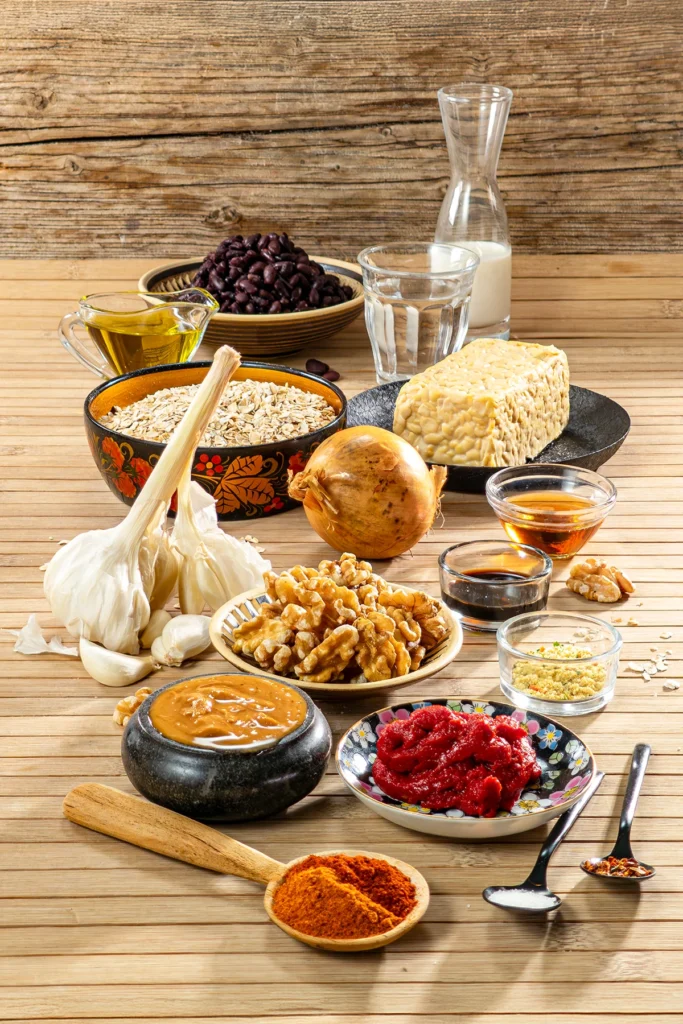 Ingredients for vegan BBQ Tempeh Burger patties, including tempeh, black beans, rolled oats, onion, garlic cloves, walnuts, soy cream, peanut butter, tomato paste, soy sauce, maple syrup, olive oil and spices.